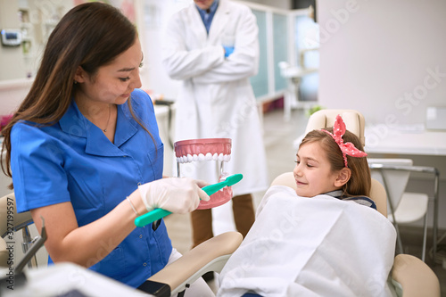 Dentist showing to child on jaw model how to brushing her teeth