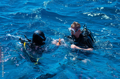 Two professional scuba divers making gestures at sea surface