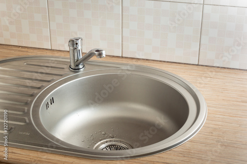 Clean round metal kitchen sink with faucet and water drops from leak