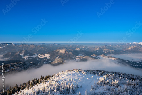 winter landscape in mountains illuminated at sunrise with fog in valley and beautiful snowy trees, slovakia Velky Choc