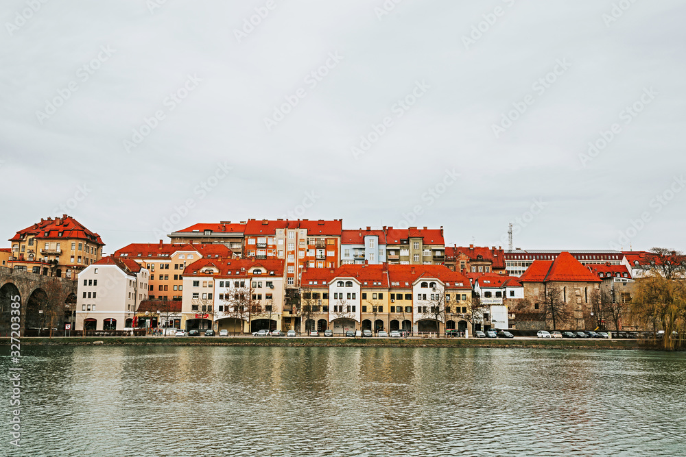 Obraz premium Houses with red roofs along the Drava River. Autumn or winter in a European city. Maribor city, Slovenia, Europe.