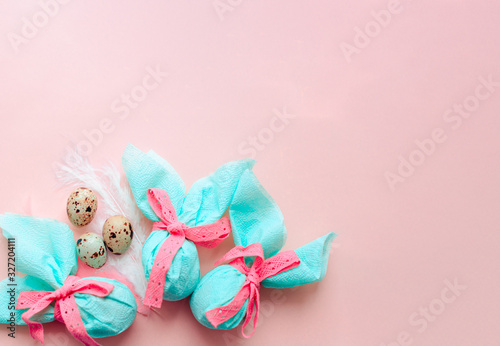Fototapeta Naklejka Na Ścianę i Meble -  Egg gift in green paper packaging and with pink ribbon Easter Bunny wrap idea. Chocolate dragee white and gold color, multicolor colorful feathers. Minimal concept. Flat lay, Copy space, top view