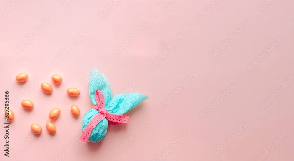 Egg gift in green paper packaging and with pink ribbon Easter Bunny wrap idea. Chocolate dragee white and gold color, multicolor colorful feathers. Minimal concept. Flat lay, Copy space, top view