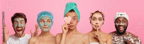 People and beauty concept. Emotional man goes crazy, applies clay mask, three women stand shoulder to shoulder, enjoy cosmetic treatment, hold sponge. Afro American guy washes body with foaming gel