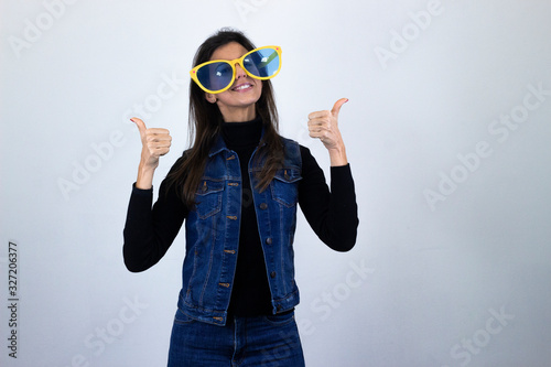 pretty  middle age woman model with big glasses showing thumbs up gesture, isolated on gray background studio shotblack sweater, denim jacket, jeans. Place for your text in copy space. photo