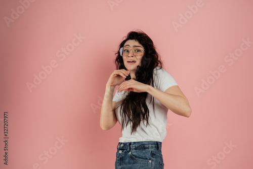 Young girl in glasses on a pink background, she is scared.Human emotions