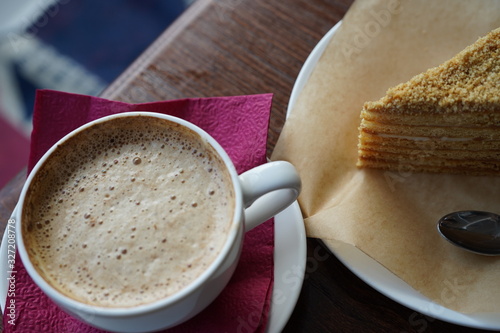 Breakfast, a Cup of cappuccino and a slice of honey cake on a white saucer with small spoon