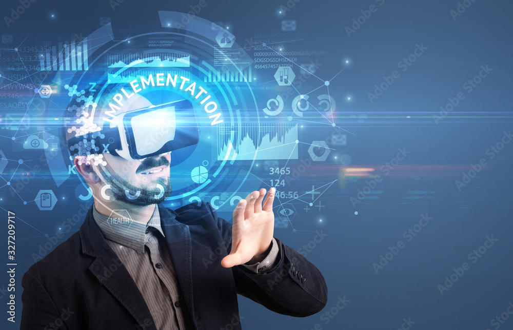 Businessman looking through Virtual Reality glasses with IMPLEMENTATION inscription, innovative technology concept Businessman looking through Virtual Reality glasses with IMPLEMENTATION inscription, innovative technology concept