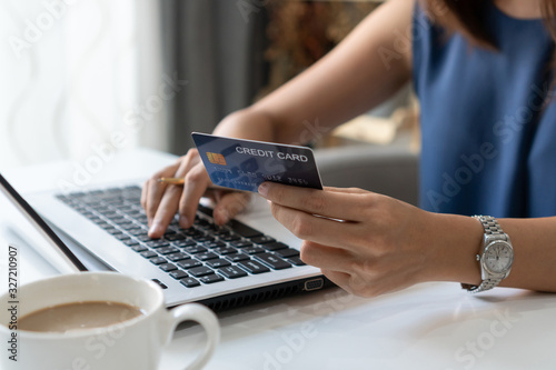 Smiling young Asian woman holding credit card while using computer laptop at home office, digital lifestyle with technology, e-commerce, shopping online concept.