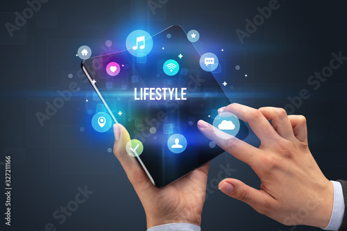 Businessman holding a foldable smartphone with LIFESTYLE inscription, social media concept