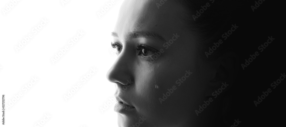 Black and white portrait of beautiful young woman with sad big eyes crying. White background. Free space for text. Tear on cheek of unhappy female. Black and white portrait of beautiful young woman with sad big eyes crying. White background. Free space for text. Tear on cheek of unhappy female.