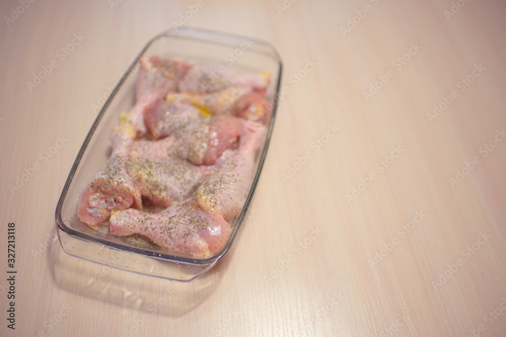 Raw chicken legs in a glass baking dish on a milk wooden table.