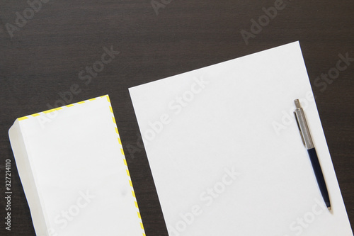 Template of white paper with pen and envelope on dark wenge color wooden background.