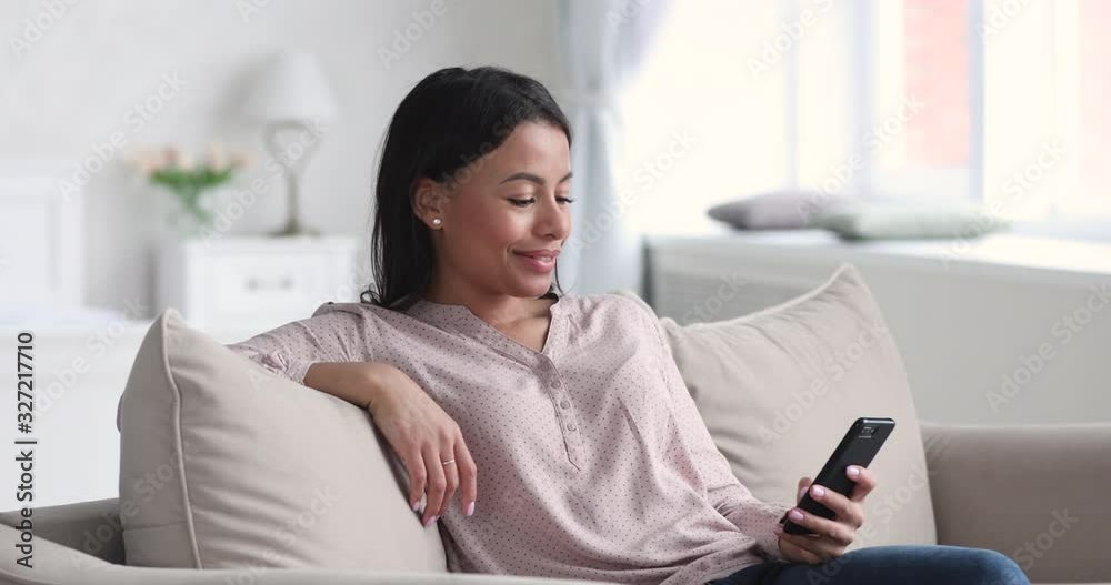 Smiling relaxed african young woman using smart phone on sofa Smiling relaxed african young woman using smart phone on sofa