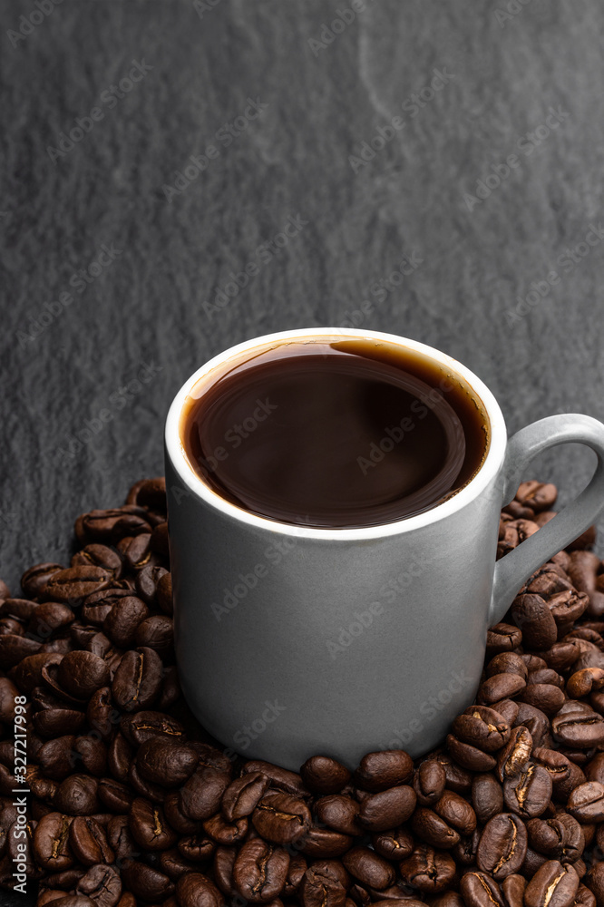 Fototapeta premium Black coffee in small cup with beans on black stone background
