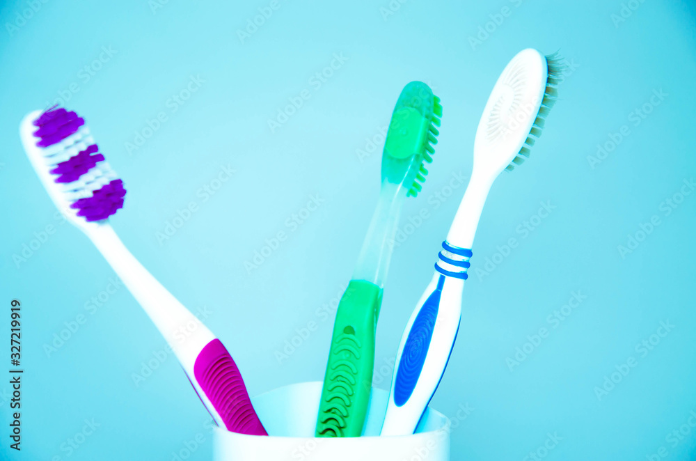 Three brushes for cleaning teeth in a glass white and orange on a blue background. Shaving machines in a glass. Brushes and machine tools in one glass on a blue background.Copy Space Three brushes for cleaning teeth in a glass white and orange on a blue background. Shaving machines in a glass. Brushes and machine tools in one glass on a blue background.Copy Space