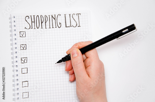 Shopping list. Hand holds a pen. Squared notebook with black pen on a white background. Record ideas, notes, plans, tasks. The list includes bread, milk, bananas.