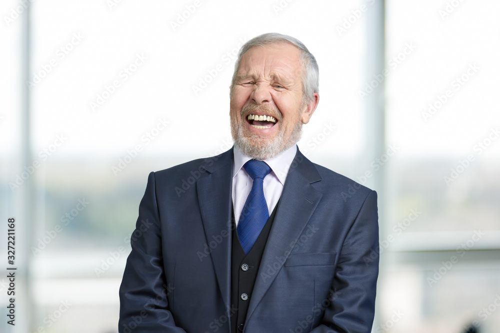 Old manager in office laughing hard. Cheerful boss in business suit portrait. Blurred windows background. Old manager in office laughing hard. Cheerful boss in business suit portrait. Blurred windows background.