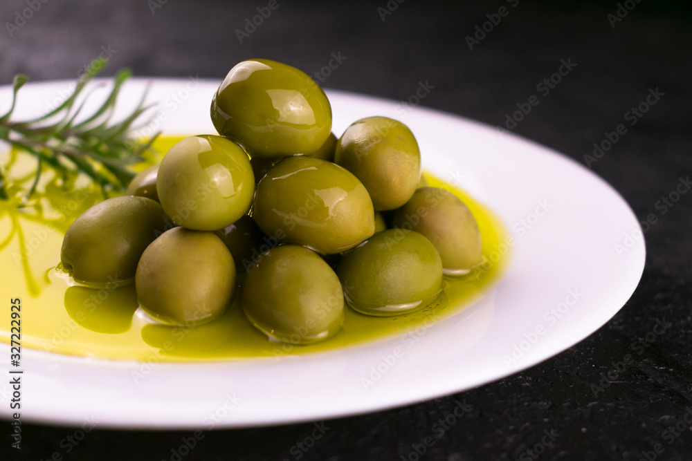 Green olives and olive oil with rosemary in a white plate on a black background. Green olives and olive oil with rosemary in a white plate on a black background.