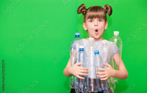 Photo of confused funny little girl holding plastic bottles and looking at camera isolated over green background
