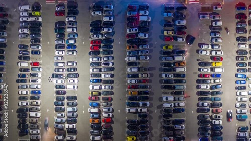 Aerial hyper lapse, top down view of supermarket (hypermarket or shopping mall) parking lot with a lots of cars at night. Time lapse photo