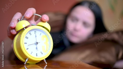 Morning. The alarm clock rings on the bedside table, the girl wakes up in bed and turns off the alarm clock and gets up. New day