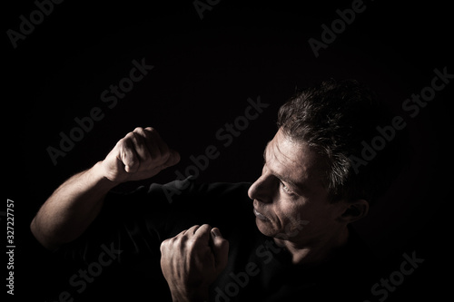 Low key profile portrait of caucasian man with clenched fists, black bacground