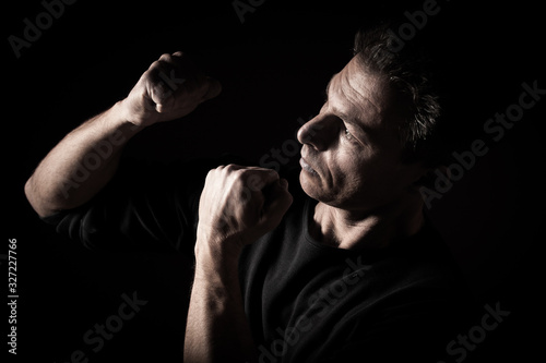 Low key profile portrait of caucasian man with clenched fists, black bacground