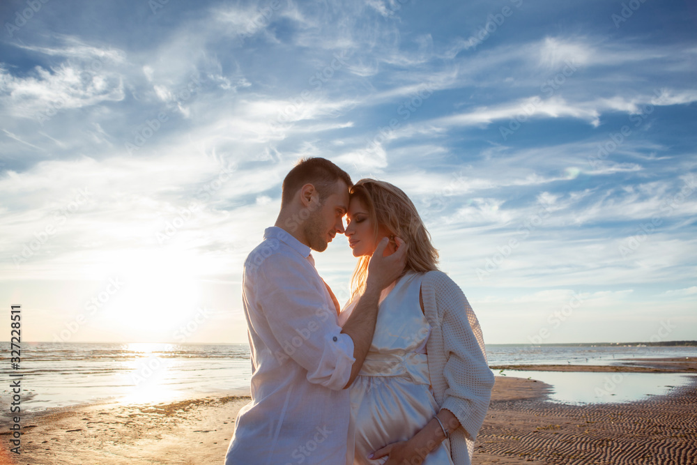 Love, romance, walk. Airy portrait of beautiful couple kissing on background of sunset sea, sandy beach and clouds.