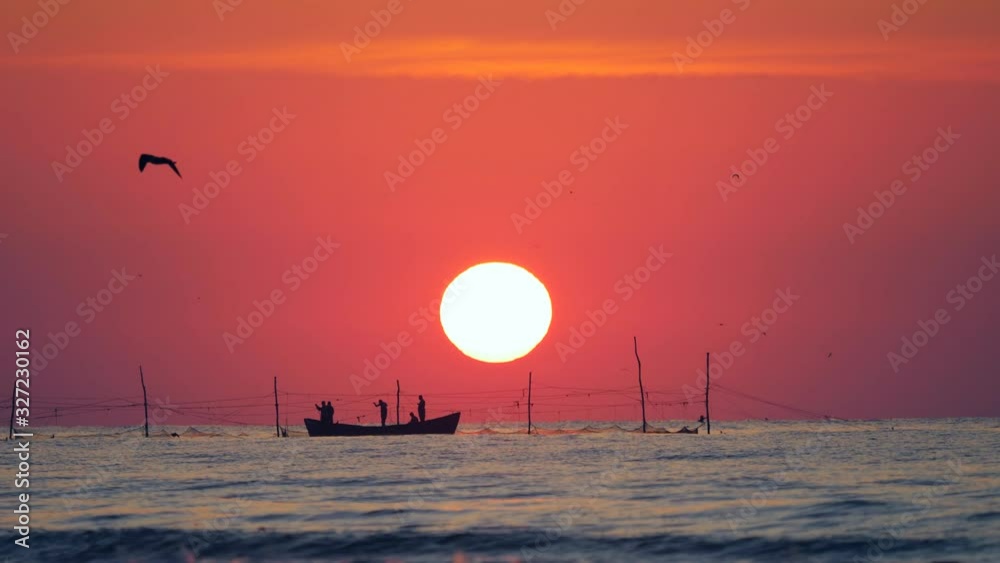 Silhouettes of men fishing on boat, red sky at sunrise