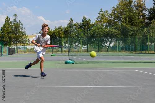 Boy tennis player runs on the court and looks at the ball. Children athletes. Young tennis player in action. Kids tournament, match. Sport concept. Space for text.