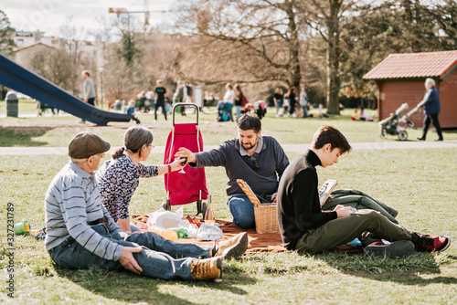 Multigenerational family having lunch at picnic in park outdoors at bright sunny spring day. Spring lifestyle. Leisure weekend activity.