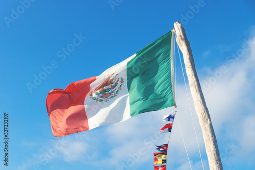 Mexican flag with small European flags on blue sunny sky