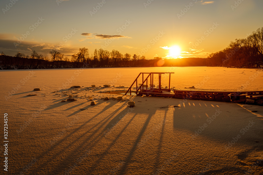 Silhouette of the pier with long shadows at sunset over frozen river