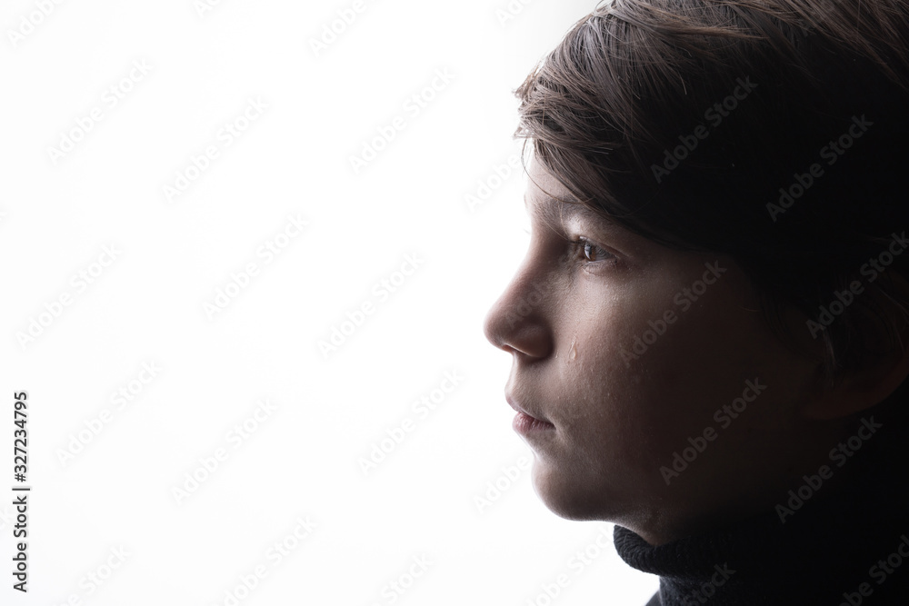 Young sad boy crying with sad eyes. White background. Free space for text. Tear on cheek of unhappy teenager.