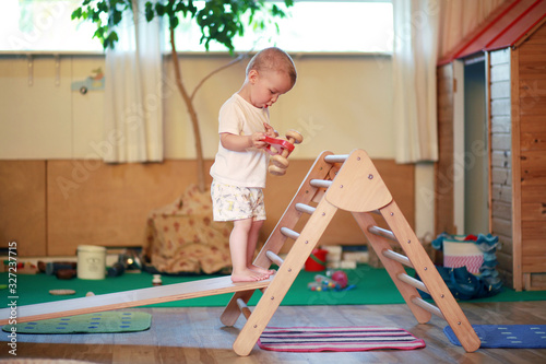 Child standing on a Pikler triangle with a red toy car in a playroom