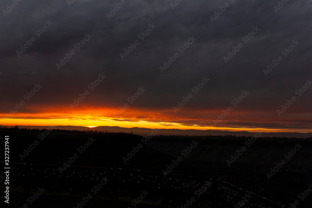 bright orange sunset with dark clouds and valley background