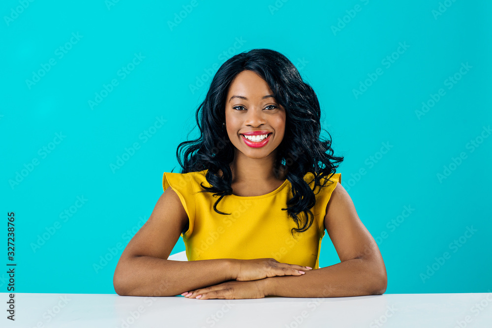© Carlos David - Portrait of a happy young smiling woman sitting behind desk  with arms crossed isolated on blue