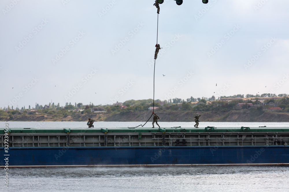 Soldiers descend from a helicopter to a barge