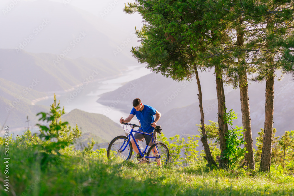 Naklejka premium Mountain biker wearing a blue shirt is pushing his bike through green woods while enjoying the amazing view.