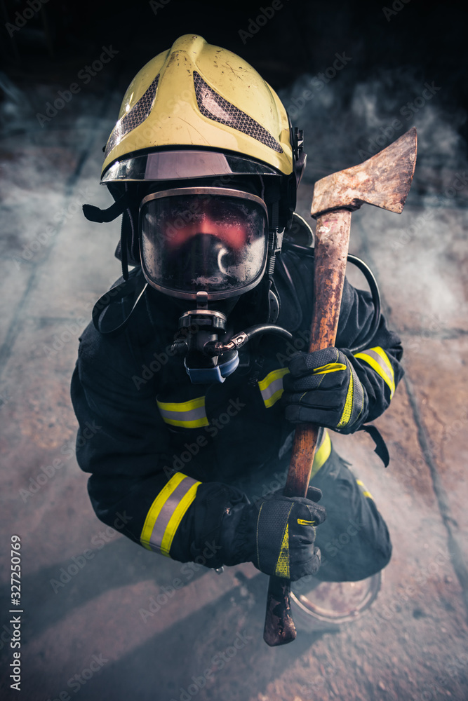 Portrait of a female firefighter while holding an axe and wearing an oxygen mask indoors surrounded by smoke.