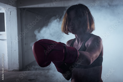 Sporty girl with a competitive fight attitude doing boxing exercises and making a direct hit on smoky background © qunica.com