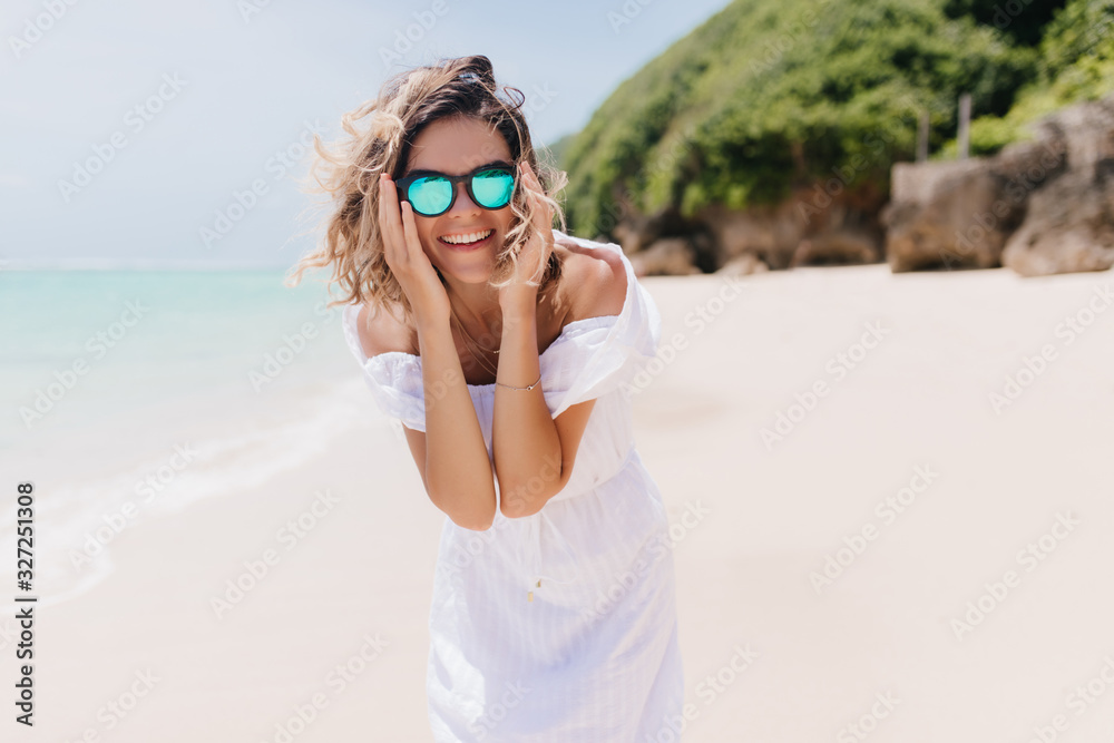 Caucasian positive girl having fun during summer weekend at resort. Good-humoured young woman expressing happiness during photoshoot at island.