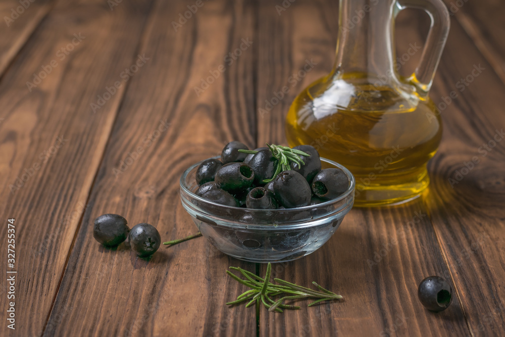 Canned olives in a glass bowl and a bottle of olive oil on a wooden table. Canned olives in a glass bowl and a bottle of olive oil on a wooden table.