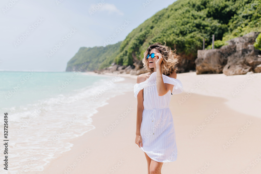 Fashionable girl in white outfit spending time at tropical island. Outdoor portrait of charming blonde woman enjoying nature views at resort. Fashionable girl in white outfit spending time at tropical island. Outdoor portrait of charming blonde woman enjoying nature views at resort.