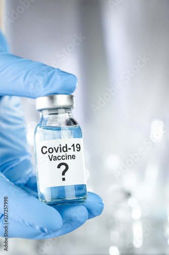 Possible cure concept with a hand in blue medical gloves holding Coronavirus, Covid 19 virus, vaccine vial