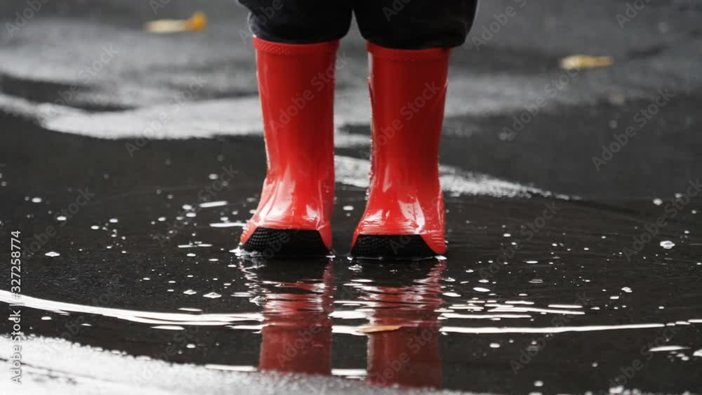 Detail of red rubber boots splashing muddle water, easy and free childhood