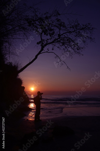 A man standing with a camera on a cliff by the sea at sunrise