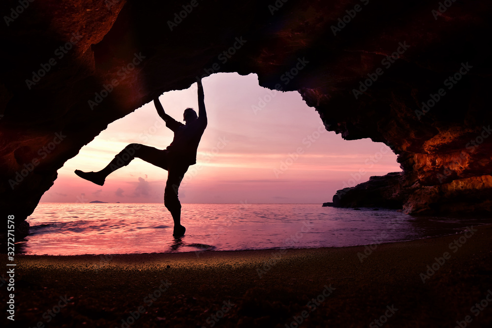 Φωτογραφία Man climbing in the cave by the beach in the morning at sunrise