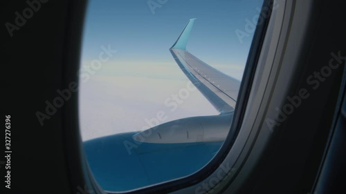 Handheld shot op jet's porthole, view. Blue Plane Wing of unrecognisable jet POV